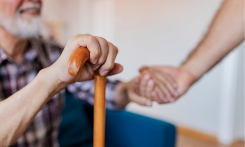 Frailty patient with walking stick holding clinician's hand